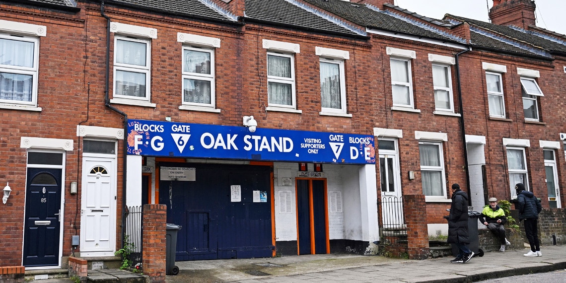 People sit by the entrance of the Oak Stand entrance at the Luton Town's Kenilworth Road stadium, in Luton