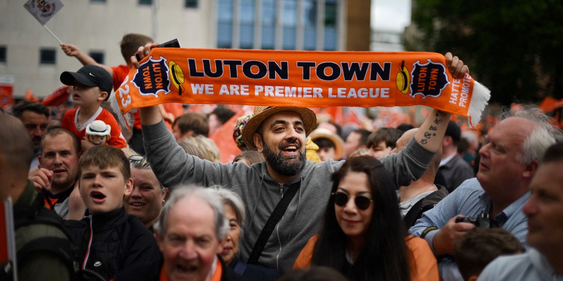 Supporters hold up placards and flags as they gather to welcome Luton Town football club players and staff at the start of a parade through the streets of Luton