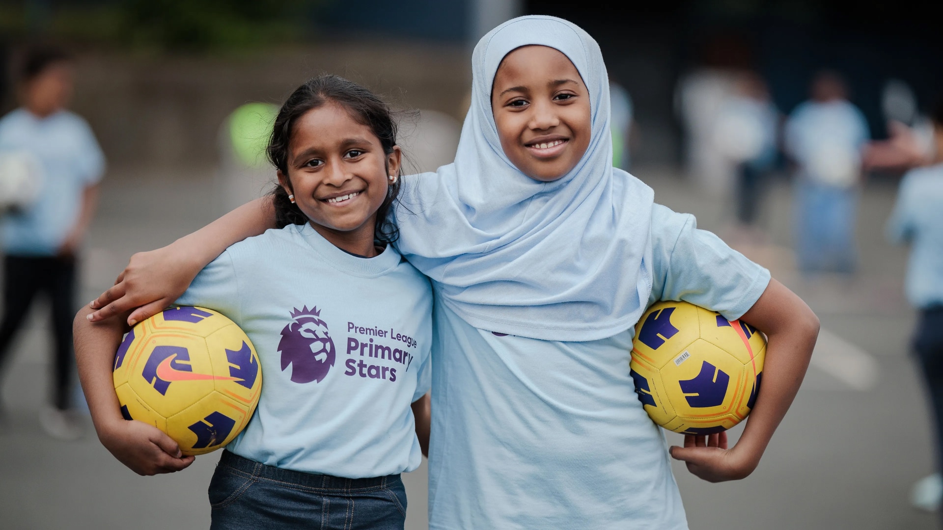 Two primary school girls holding footballs and smiling at the camera